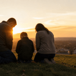 Family kneeling in prayer at sunrise overlooking an American town, symbolizing National Day of Prayer and faith across generations