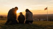 Family kneeling in prayer at sunrise overlooking an American town, symbolizing National Day of Prayer and faith across generations