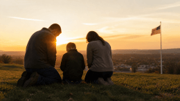 Family kneeling in prayer at sunrise overlooking an American town, symbolizing National Day of Prayer and faith across generations