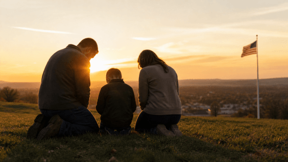 Family kneeling in prayer at sunrise overlooking an American town, symbolizing National Day of Prayer and faith across generations