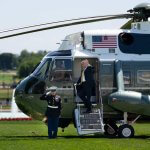 President Donald Trump waves from the steps of Marine One on the South Lawn of the White House, May 12, 2026, departing for a state visit to Beijing as a U.S. Marine renders honors with the Jefferson Memorial in the distance.