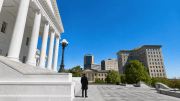 A lone watchman in a dark overcoat stands on the steps of the Virginia State Capitol, looking out over the city of Richmond.
